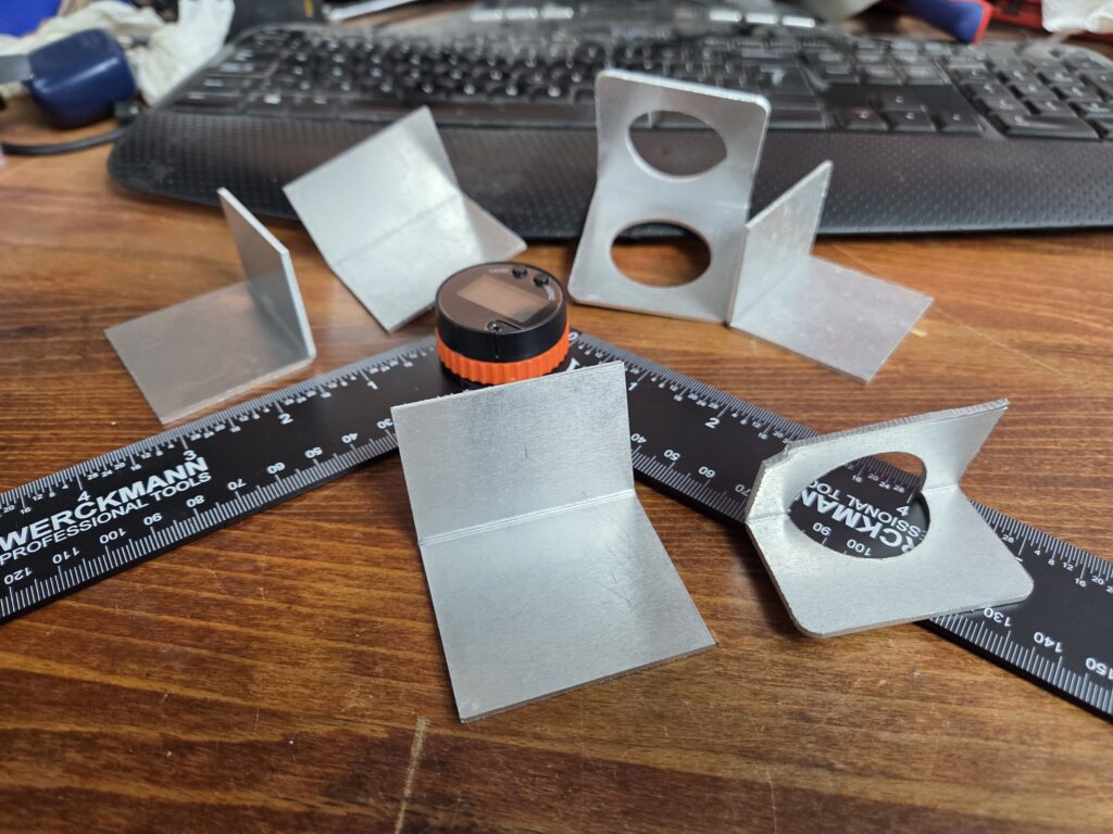 Fiber-laser-cut steel brackets bent into finished parts, measured with a ruler and digital angle gauge