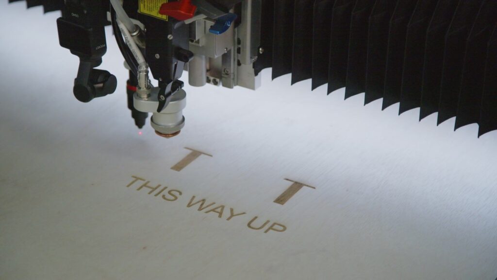 Laser engraving THIS WAY UP shipping markings into a plywood crate panel