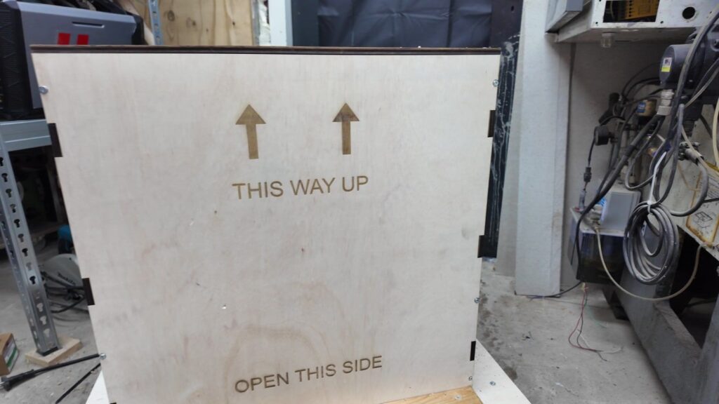 Finished laser-cut plywood shipping crate with engraved THIS WAY UP and OPEN THIS SIDE markings